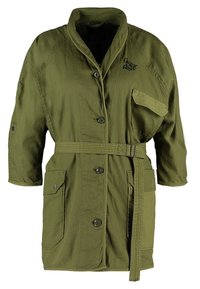 Olive green, belted utility jacket with a pointed collar, two front pockets, and button closure. Features textured fabric and logo detail.