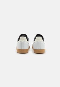 Vita skor med svarta accenter, med en slät läderfinish, rundad form och gummigummisulor. Subtil sömnadsdetalj synlig.