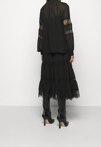Schwarzes, geschichtetes Kleid mit Spitzenrand, durchsichtigen Ärmeln und lockerer Passform. Knielange schwarze Stiefeletten mit Absatz vervollständigen den Look.