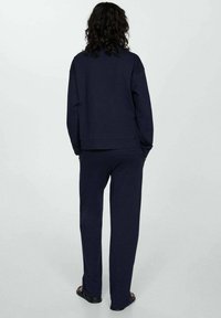 Granatowy dres składający się z luźnej bluzy i dopasowanych spodni, wykonany z miękkiej, teksturowanej tkaniny o minimalistycznym designie.