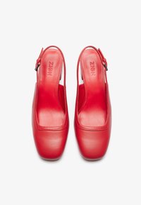 Scarpe slingback di pelle rossa con punta quadrata e texture liscia. Comprendono una cerniera laterale per la chiusura e un logo impresso sulla soletta.