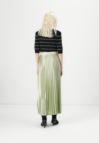 Haut à manches courtes noir et blanc rayé associé à une longue jupe plissée brillante de couleur vert clair, porté avec des bottines noires.