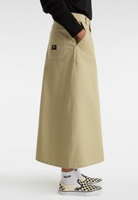 Beige lång kjol med en figurnära midja, sidfickor och kontrasterande sömmar. I kombination med svart och vit rutiga slip-on skor.