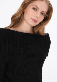 Fekete, váll nélküli pulóver bordázott kivágással. Puha, texturált anyag. Testhezálló fazon finom varrási részletekkel.