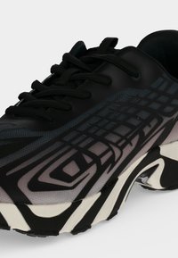Chaussure de sport noire et grise avec des lacets noirs et un design à motifs sur le côté, avec une semelle épaisse blanche et noire.