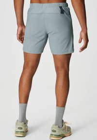 Helle graue Sportshorts mit elastischem Bund, einer Gesäßtasche und glattem Stoff. Getragen mit grauen Socken und gedämpften grünen Turnschuhen.