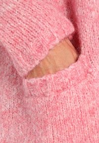 Pink knitted sweater fabric with a soft, textured finish. Features a hand pocket on the side, showcasing a loose fit and ribbed detailing.