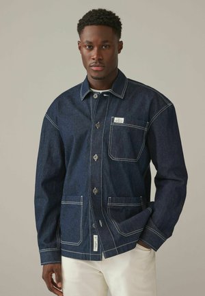 Dark denim jacket featuring a button-up front, pointed collar, and contrast stitching. Includes a chest pocket and two front pockets.