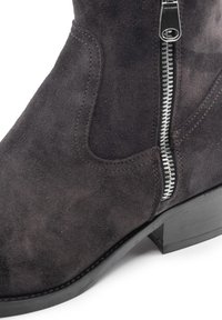 Stivale alla caviglia in suede grigio scuro con zip laterale, texture liscia, punta tonda e tacco basso impilato. Dettagli cuciti visibili vicino alla cerniera.