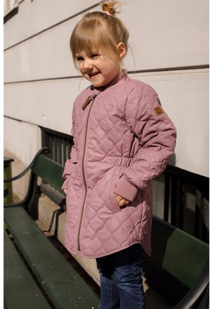 Gewatteerd, lichtroze jack met een ritssluiting, geribbelde manchetten en een decoratief embleem op de mouw, gedragen over een blauwe spijkerbroek.