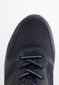 Marinblå sportskor med ovandel i mesh och släta läderdetaljer. Utrustad med blå snören och en förstärkt tå. Texturerad yta synlig.