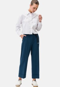 Witte overhemd met knoopsluiting en een zak, gecombineerd met marineblauwe wijde broek met een koord en cuffs, en witte sneakers.
