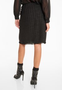 Schwarzer Tweed-Rock mit strukturierter Oberfläche, Fransen-Saum und mittellanger Schnittführung. Kombiniert mit schwarzen, hochhackigen Stiefeletten und schwarzen Socken.