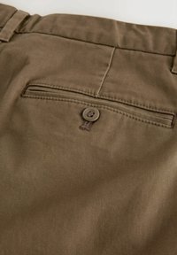 Brown chinos with a smooth, textured fabric feature a rear pocket with a button closure and contrasting stitching.
