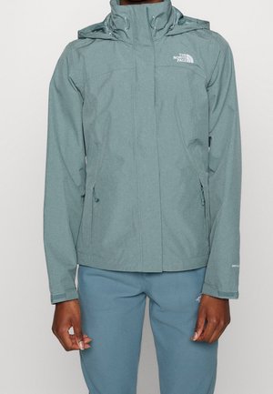 Person wearing a muted blue-green North Face hooded jacket and matching pants standing against a plain light background.