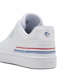 Vit Puma-sko med röda, mörkblå och ljusblå ränder på sidan och en cirkulär BMW-logga på hälen.