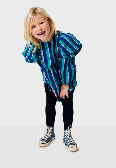 Abito blu e verde a righe con maniche a sbuffo, abbinato a leggings neri e sneakers blu. L'abito presenta una vestibilità ampia e un orlo curvo.