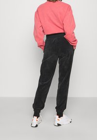 Röd sweatshirt med ribbade mudd, tillsammans med svarta kordbyxor med elastisk midja. Vita sneakers med orange detaljer.