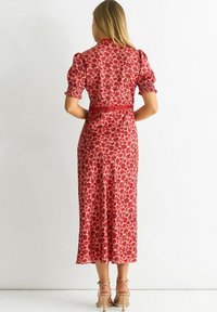 Red floral-patterned dress with puff sleeves and a fitted waist. Mid-calf length, soft fabric, and subtle sheen. Paired with nude strappy heels.