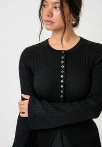 Schwarzer Rippstrick-Cardigan mit langen Ärmeln und rundem Ausschnitt, der vorne mit acht Knopfverschlüssen geschlossen wird und eine taillierte Silhouette hat.