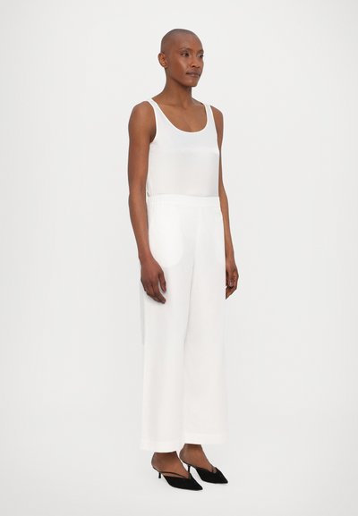 Valge ilma varrukateta top, laiad valged püksid elastse vööga ja mustad terava ninaga kingad. Sile kangas ja mugav lõike.