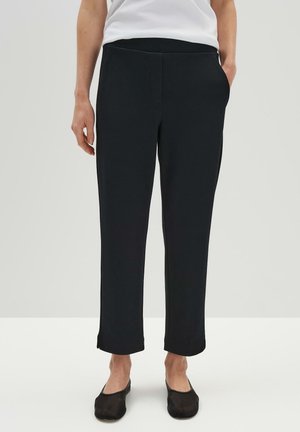 Pantalon noir texturé avec une coupe droite, doté de poches latérales et d'une taille confortable, associé à des chaussures plates noires.