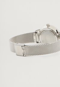 Ρολόι με ασημένιο πλέγμα λουριού, στρογγυλή θήκη, λεία επιφάνεια και κλείσιμο με κούμπωμα. Αδιάβροχο με χάραξη στην πίσω πλευρά.