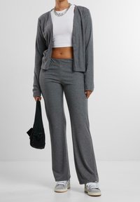 Šedý žebrovaný kardigan přes bílou zkrácenou tílko, doplněný o odpovídající šedé kalhoty a černou tašku. Tenisky mají šedou, bílou a béžovou barvu.