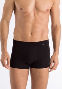 Black cotton boxer shorts with a fitted design, elastic waistband, and a contrast stitching detail. Material appears smooth and stretchy.