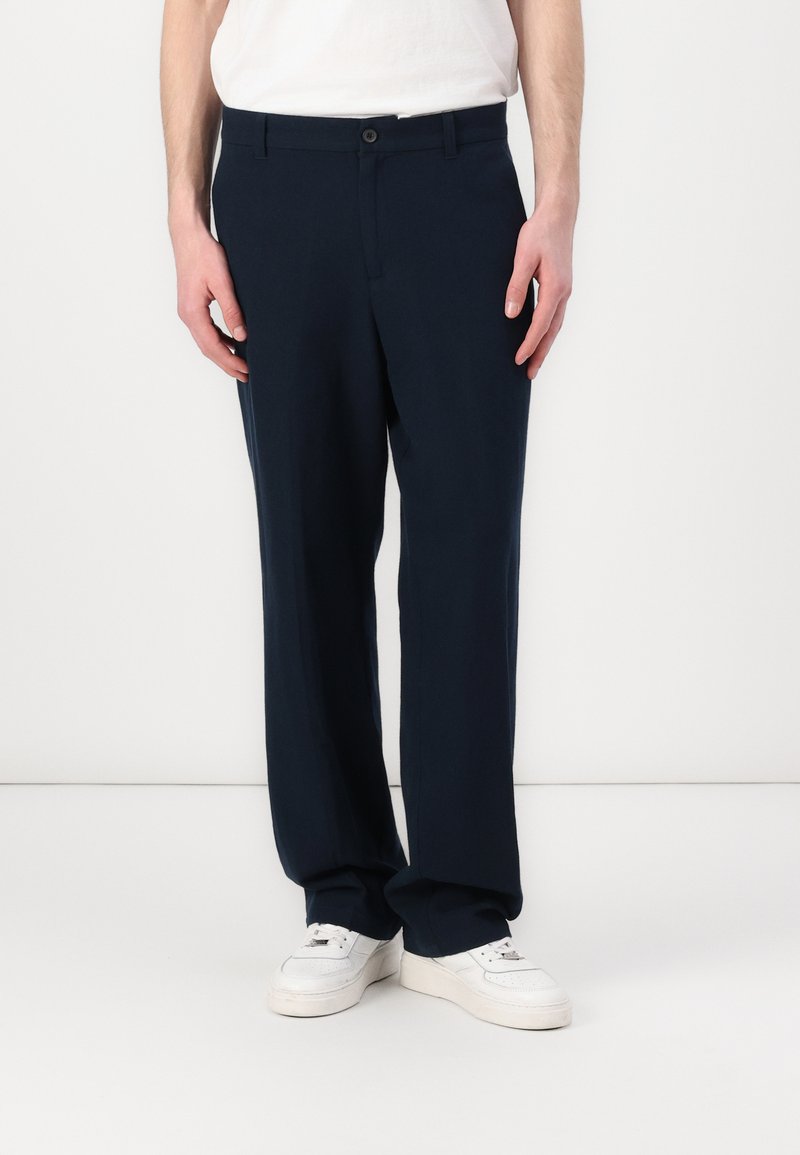 Navy blue, lightweight trousers with a straight fit, featuring a button closure and slanted pockets, paired with white sneakers.