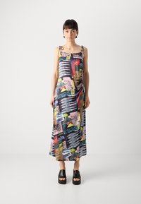 Abito lungo in satin con stampe grafiche multicolori, sottili spalline a spaghetti e una silhouette fluida, abbinato a sandali neri con plateau.