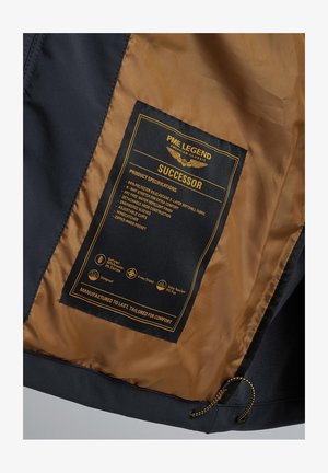 Wnętrze kurtki softshell z czarnym zewnętrzem i brązowym wykończeniem, z metką zawierającą specyfikacje produktu oraz instrukcje pielęgnacji.