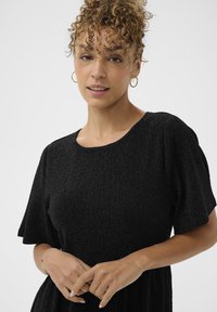 Vestido negro texturizado con mangas cortas abullonadas y escote redondo. Presenta patrones sutiles y un diseño fluido.