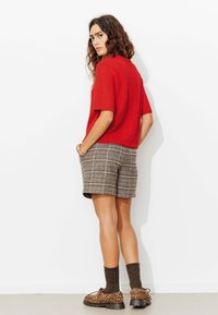 Pull rouge à manches courtes associé à un short à carreaux marron. Les accessoires comprennent un bracelet en or et des chaussures à imprimé animalier avec des chaussettes foncées.