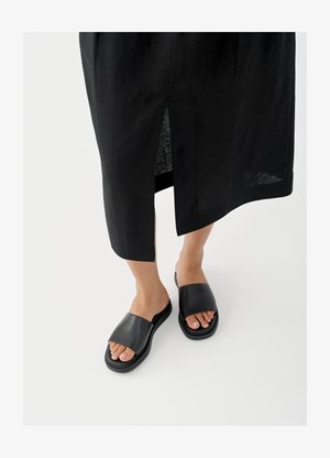 Čierne šľapky so širokým remienkom, plochou podrážkou a minimalistickým dizajnom. Materiál pôsobí hladko s matným povrchom.