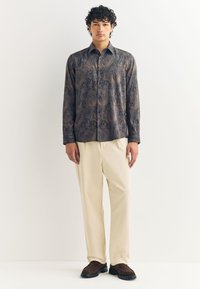 Tumesinises toonis pikakäise särk pruuni paisleilmustriga, kombineeritud beežide pükste ja pruuni tekstuurse detailiga kingadega.