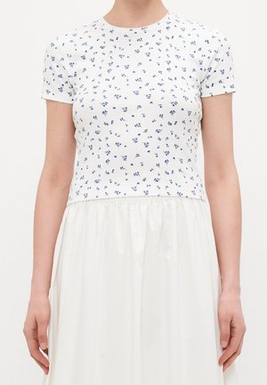 Witte aansluitende top met korte mouwen en een kleine blauwe bloemenprint, gedragen met een witte rok met hoge taille.