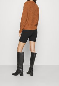 Brun stickad tröja, svarta knälånga shorts och knähöga svarta läderstövlar med fyrkantig klack. Strukturerad tyg och figurnära design.