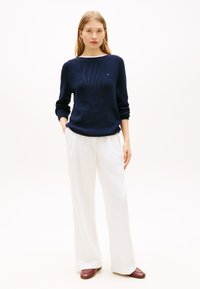 Πλεκτό πουλόβερ ναυτικού μπλε με ριμπ υφή, φαρδύ λαιμόκοψη σαν καραβάκι και μακριά μανίκια. Συνδυασμένο με λευκό παντελόνι φαρδύ και μπορντό παπούτσια.