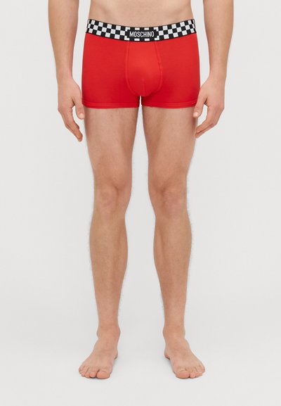Red cotton boxer briefs with a black and white checkered waistband featuring "MOSCHINO" logo. Fitted design, mid-thigh length.