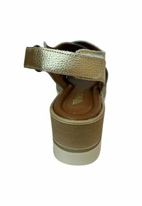 Sandalia de cuero dorado con una amplia correa en el tobillo, plataforma texturizada y plantilla acolchada marrón. Presenta un diseño de tacón bajo y robusto.