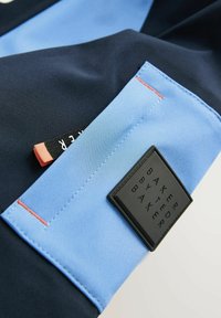 Mørkeblå og lys blå stof med en glat tekstur, der har et sort rektangulært label prægede med "BAKER BY TED BAKER" og kontrasterende orange syninger.