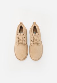 Botas de tobillo de ante beige con forro de pelo sintético, puntera redondeada, tres ojetes y una lengüeta trasera para facilitar su colocación. Textura suave en toda la superficie.