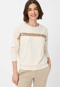 Cremefarvet sweatshirt lavet af blødt stof, med en vandret stribe af gyldne paljetter over brystet. Ribbet manchetter og kant.