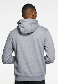 Grå huvtröja i mjukt tyg, med en logotyp på baksidan, ribbade ärmslut och en känguruficka fram.