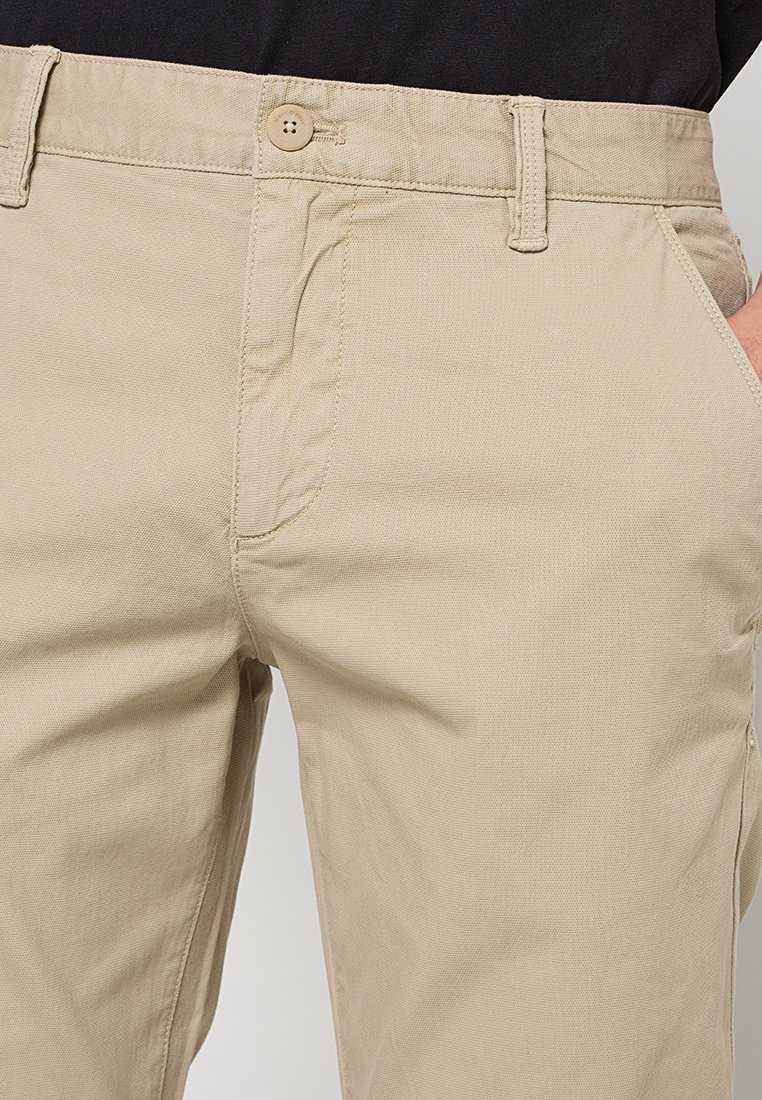 Beżowe bawełniane spodnie z fakturowanej tkaniny, z zapięciem na guzik i bocznymi kieszeniami. Prosty design z prostym krojem i szlufkami na pasek.
