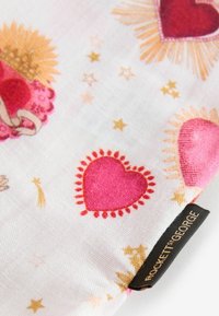 Tela blanca con corazones rosas y rojos rodeados de estrellas y rayos dorados, con una etiqueta negra con el texto "Rockett St George".