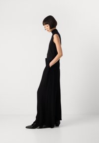 Fekete ujjatlan felső, laza fekete nadrággal párosítva. Az outfit magas nyakkal, oldalzsebekkel és elegáns fekete lábbelivel rendelkezik.