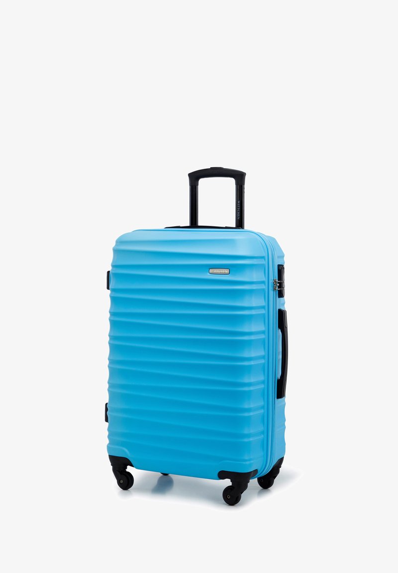 Valise rigide de couleur bleu vif, dotée de rainures verticales, d'une poignée rétractable et de quatre roues noires pour une meilleure mobilité.