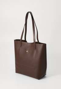 Borsa tote in pelle marrone scuro con due manici lunghi e una tasca frontale chiusa da un piccolo bottone dorato, su uno sfondo chiaro e semplice.